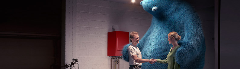 un chauffagiste et une cliente se serrent la main devant une chaudière, ils sont rassemblés par un ours bleu
