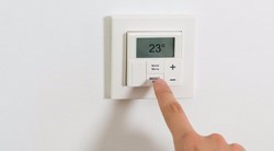 un doigt posé sur un thermostat intérieur
